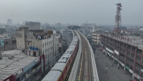 aerial drone tilt up shot over orange metro rail track beside lahore hotel building before reaching a station in lahore, pakistan