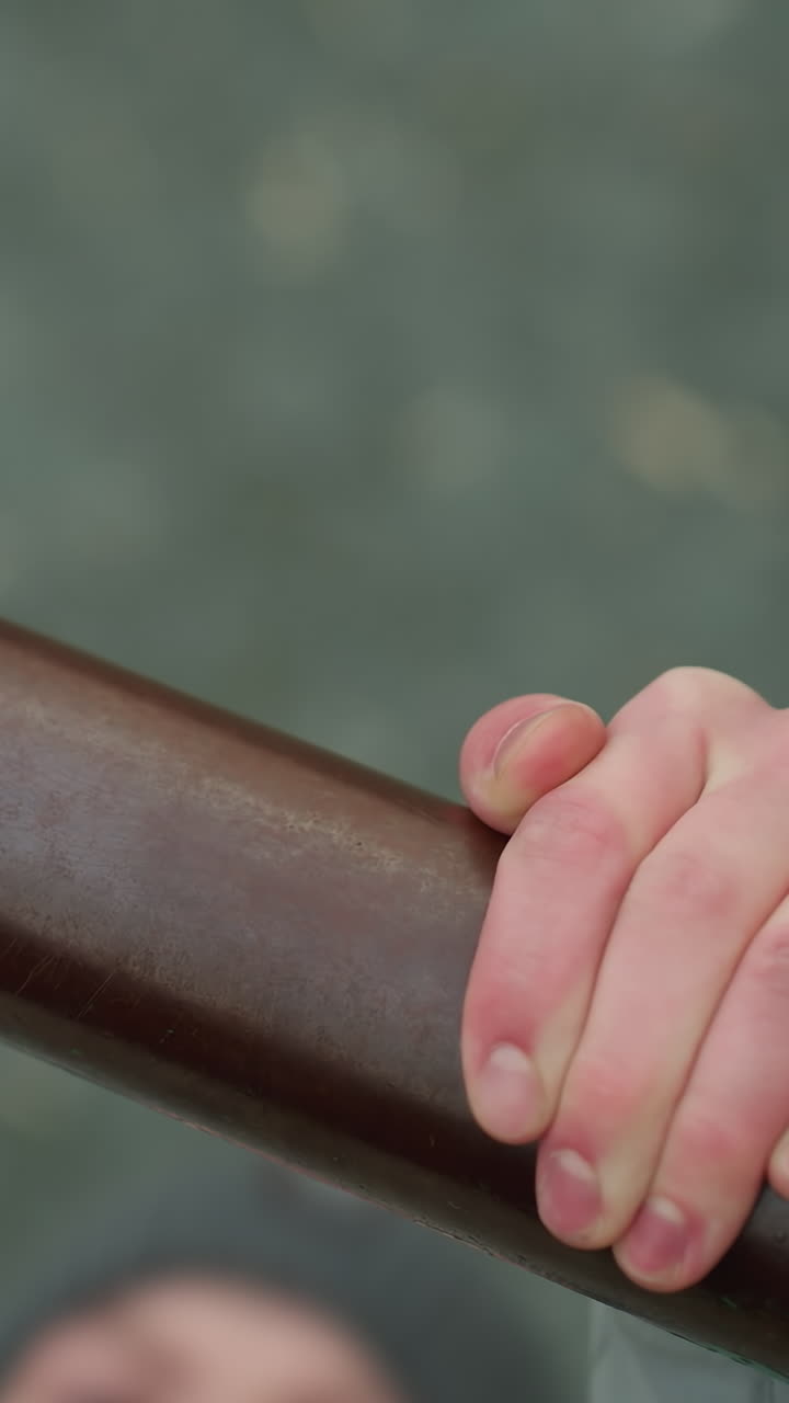 Close-up of a young boy gripping an iron bar during a workout session, with a blurred view of the boy s face and surroundings