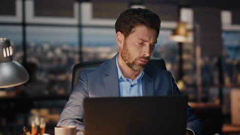 exhausted man working laptop in late night office closeup. tired businessman