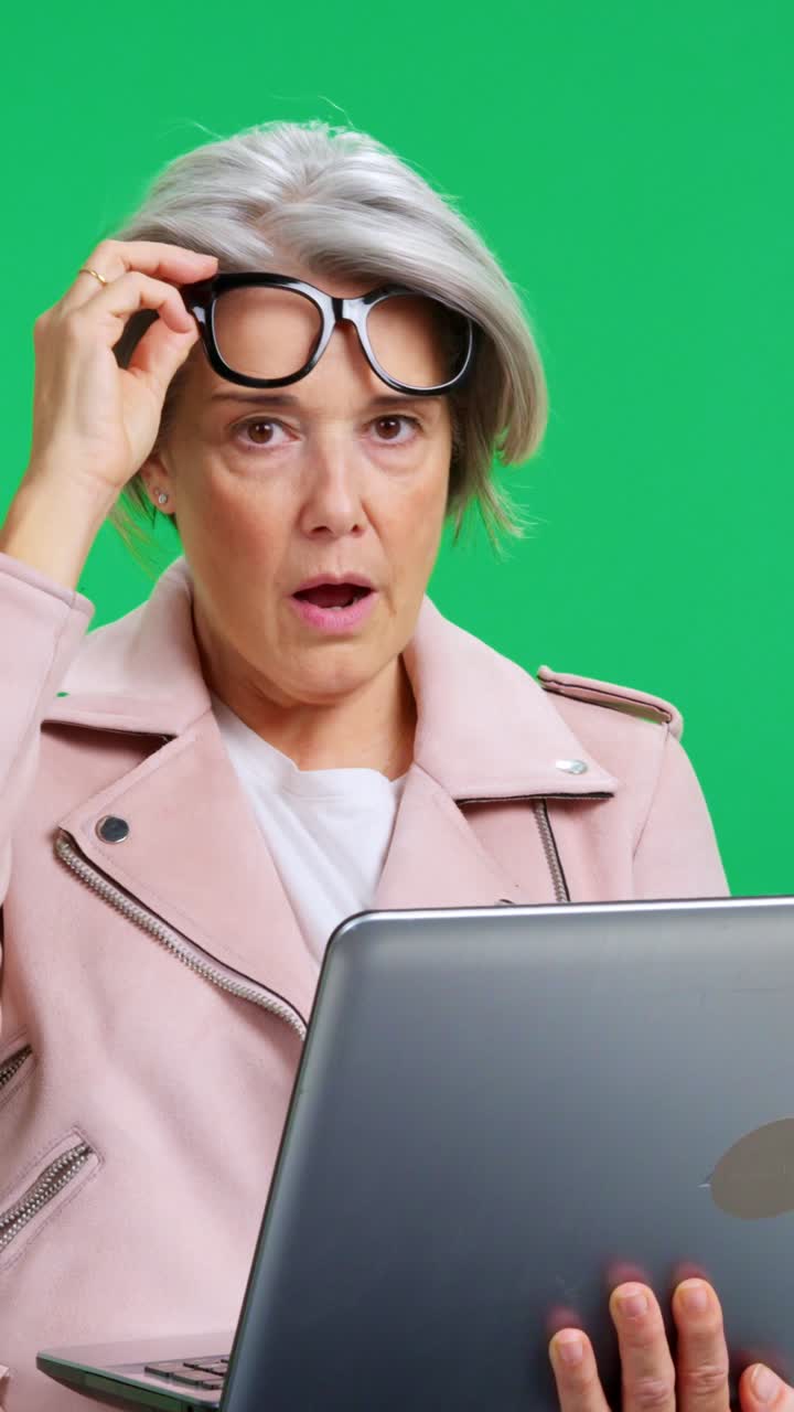 Ältere Frau reagiert schockiert und überrascht, während sie einen Laptop benutzt.