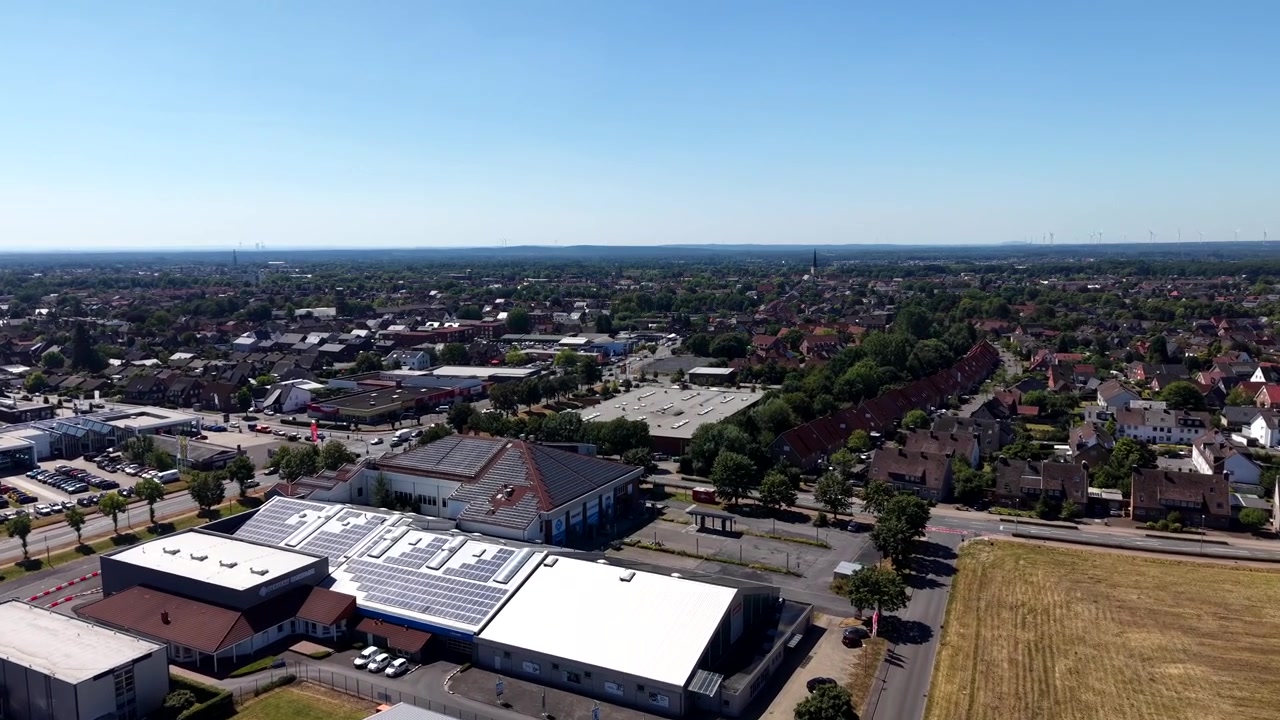 Industribygning med solpaneler på taget, der overser et lille amerikansk bykvarter med røde tage på husene, kirketårn, parkeringspladser og gyldent landbrugsland i det fjerne. Bredt luftfoto fra drone.