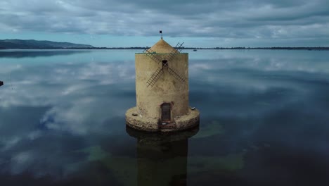 old spanish windmill in the lagoon at old island town orbetello near monte argentario and the maremma nature park in tuscany, italy, with blue sky and calm blue water