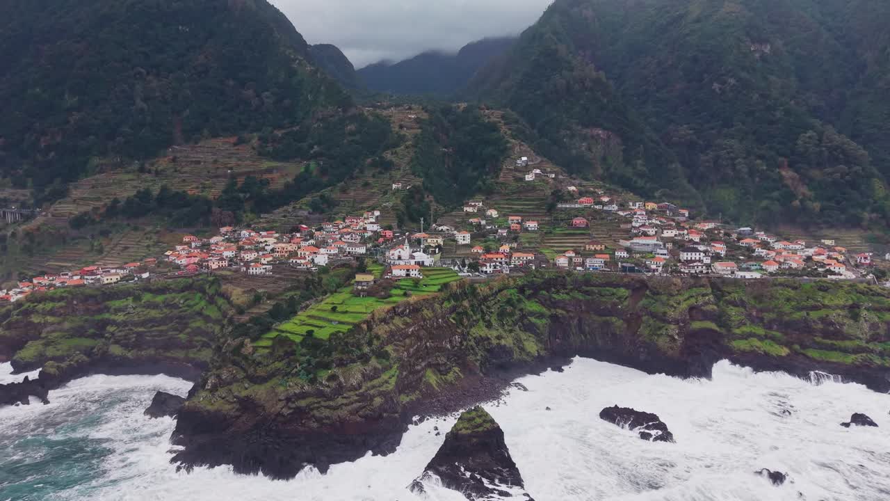 Vista aérea da vila costeira do Seixal na ilha da Madeira, empoleirada em falésias íngremes com paisagem em socalcos e poderosas ondas atlânticas ao longo da costa acidentada.