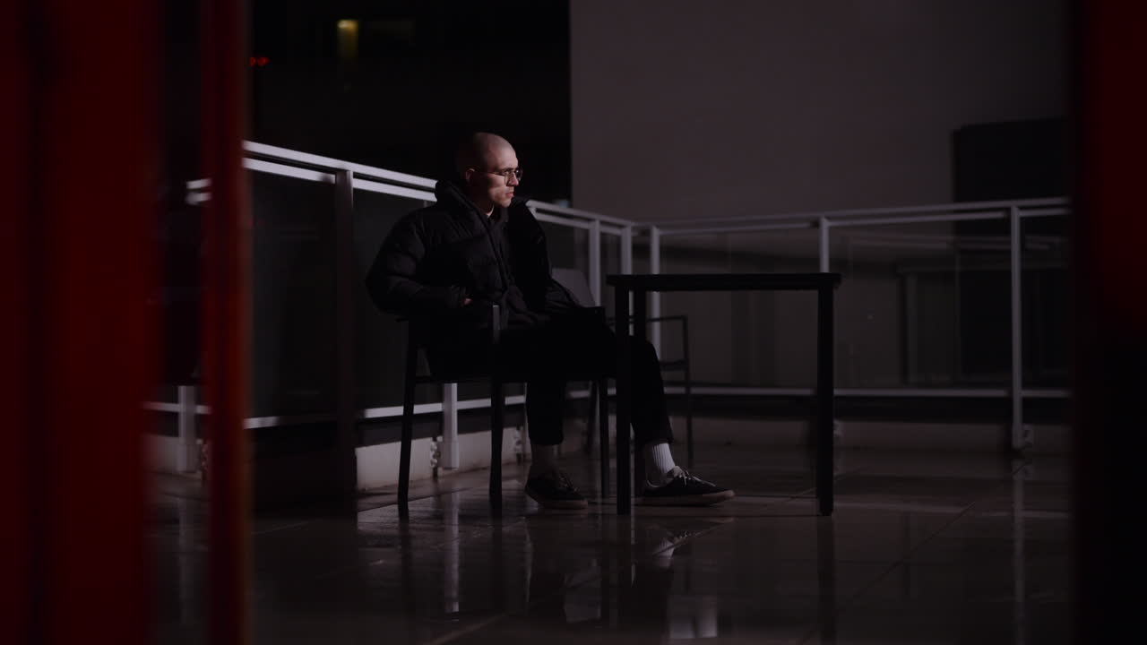 Man Sitting on a Balcony at Night Using a Smartphone