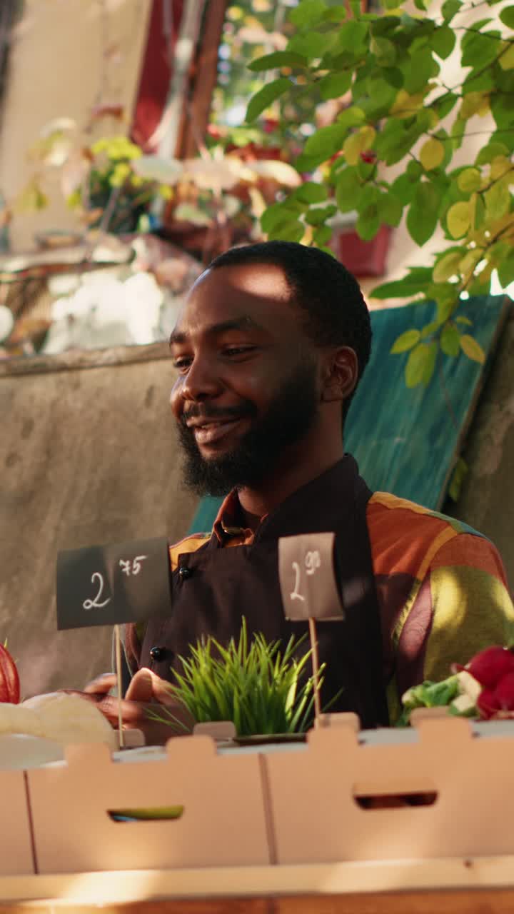 Vertical video: Young male farmer selling box of organic garden produce at local food market