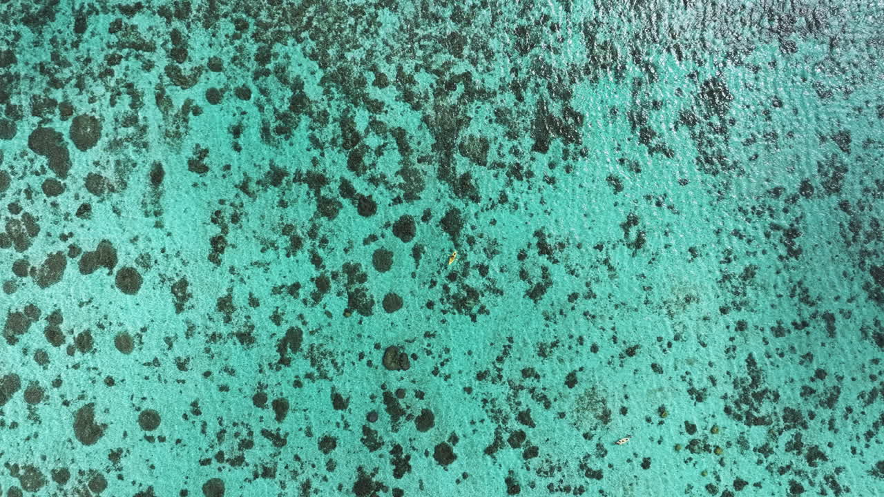 A breathtaking drone shot descending towards a kayak floating on the clear turquoise waters near the Cook Islands