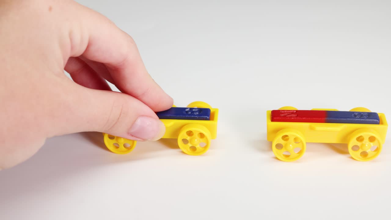 Toy cars with magnets interact on a white surface, showing magnetic attraction and repulsion. Bright lighting highlights the colorful vehicles