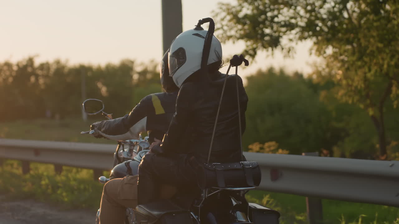 Back view of motorcycle rider moving on road with passenger, both wearing helmets and leather jackets, passing road sign, symbolizing travel, lifestyle, freedom, adventure, motion and connection