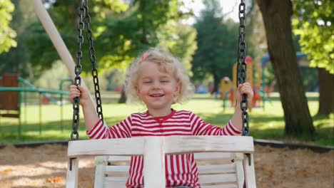 happy toddler girl smiling on a swing in a park
