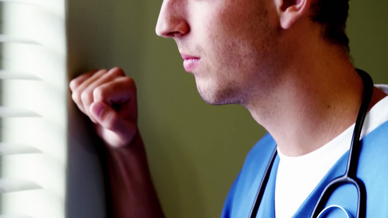 Medico pensieroso in piedi accanto alla finestra