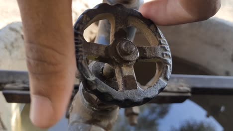 a man's hand opens a valve on a water pipe