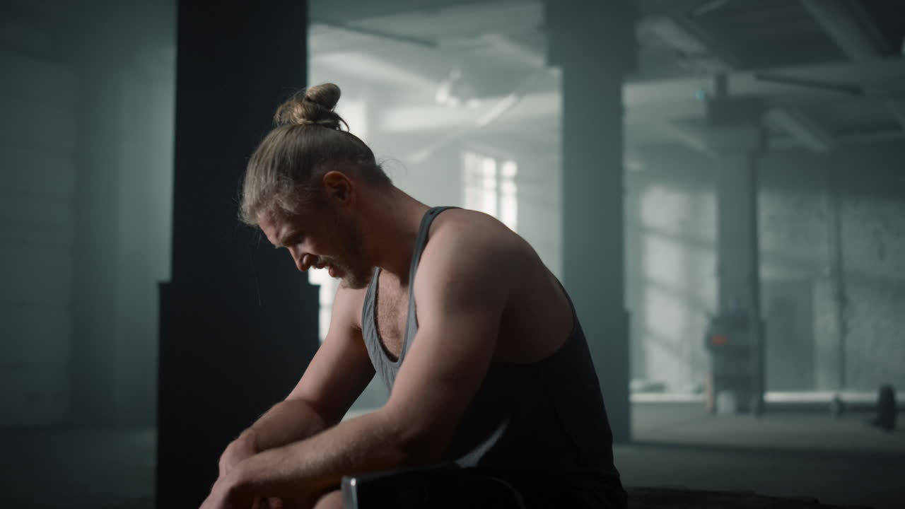 Sportsman sitting on crossfit tire. Fitness man taking break between exercises