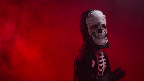 studio shot of child dressed up in skeleton costume trick or treating at halloween dancing in front of red smoke background lighting