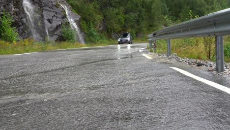 Rain-flowing-over-asphalt-in-foreground-with-parked-car-and-waterfalls-in-background---Closed-road-during-heavy-rain-and-flooding-concept