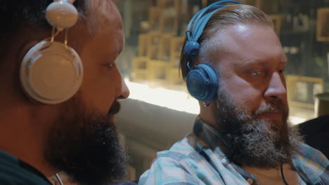 close up view of two bearded men listening musics using colorful on-ear headset