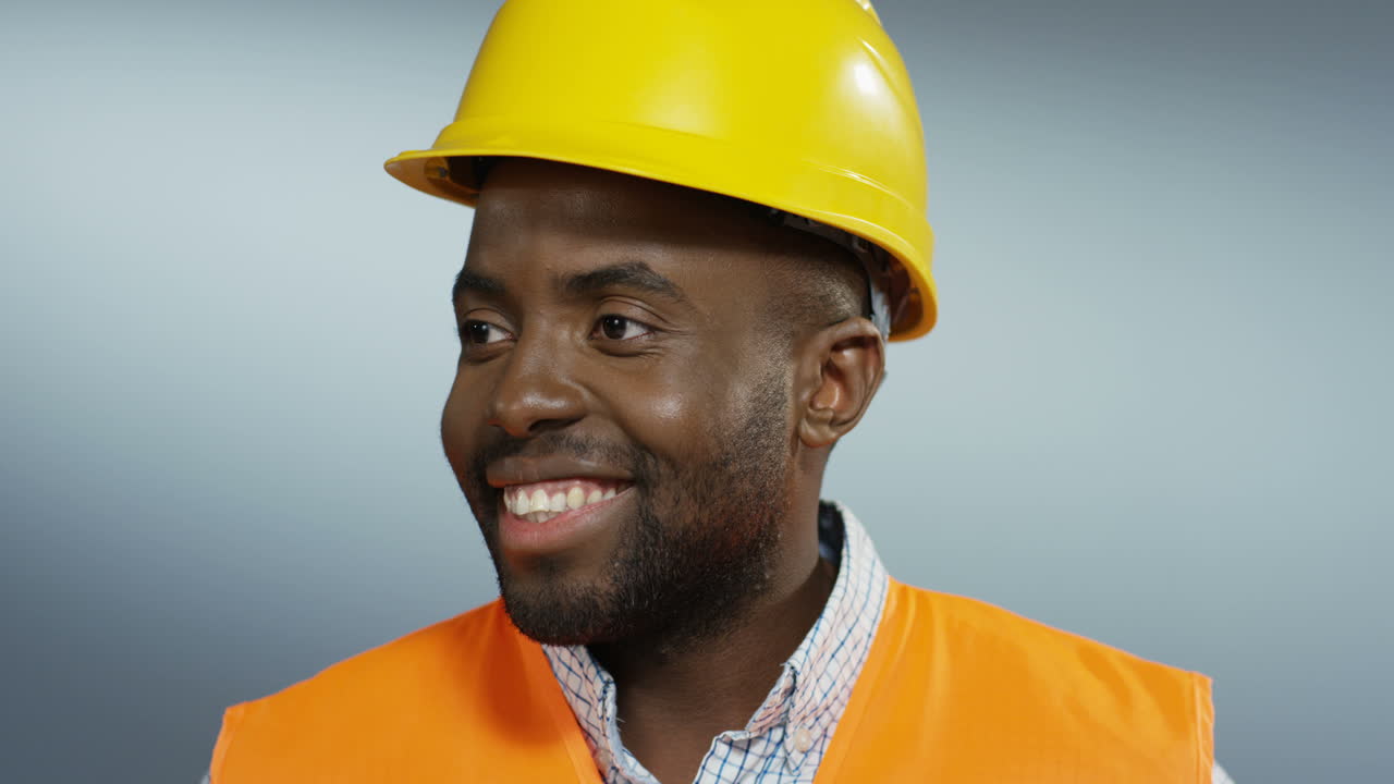 toma de retrato del apuesto joven constructor en un casco amarillo girando la cara y sonriendo a la cámara