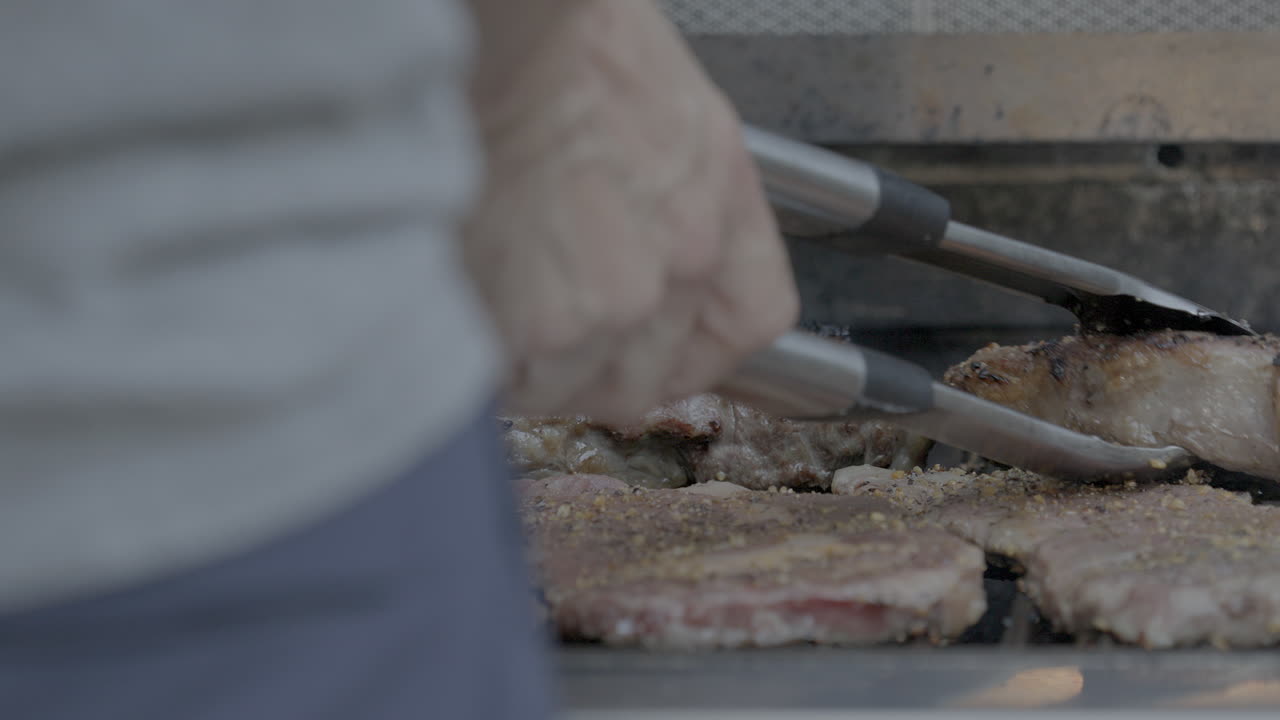 밖에서 그릴을 작업하는 요리사가 스테이크를 확인하고 그릴 뚜껑을 닫습니다.