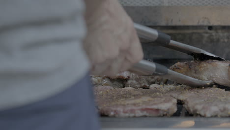 a cook working a grill outside checks on steaks and closes the grill lid