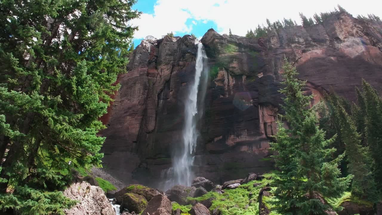 Telluride Bridal Veil Falls aerial drone Waterfall Telluride windy mist spray Black Bear Pass Road Colorado pine tree Ouray Ridgway Box Canyon cliffside 4wd hiking cloudy sun blue sky upwards jib pan