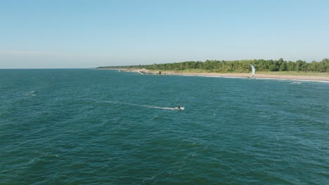 Establishing-aerial-view-of-a-group-of-people-engaged-in-kitesurfing,-sunny-summer-day,-high-waves,-extreme-sport,-Baltic-Sea-Karosta-beach-,-birdseye-drone-dolly-shot-moving-right