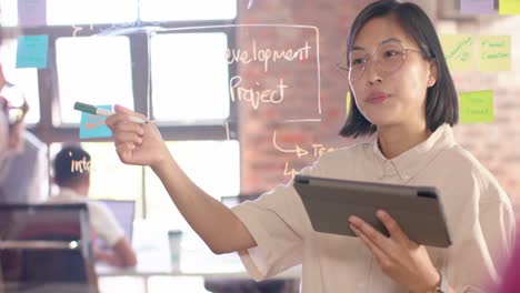 happy asian creative businesswoman with tablet brainstorming ideas at glass wall, slow motion