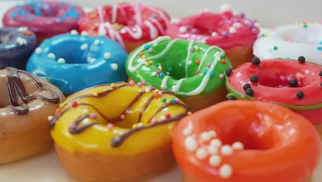 lush, round pastries - donuts with multi-colored glaze lie on a white table, covered with white-dark chocolate with colored sprinkles. sweets close-up