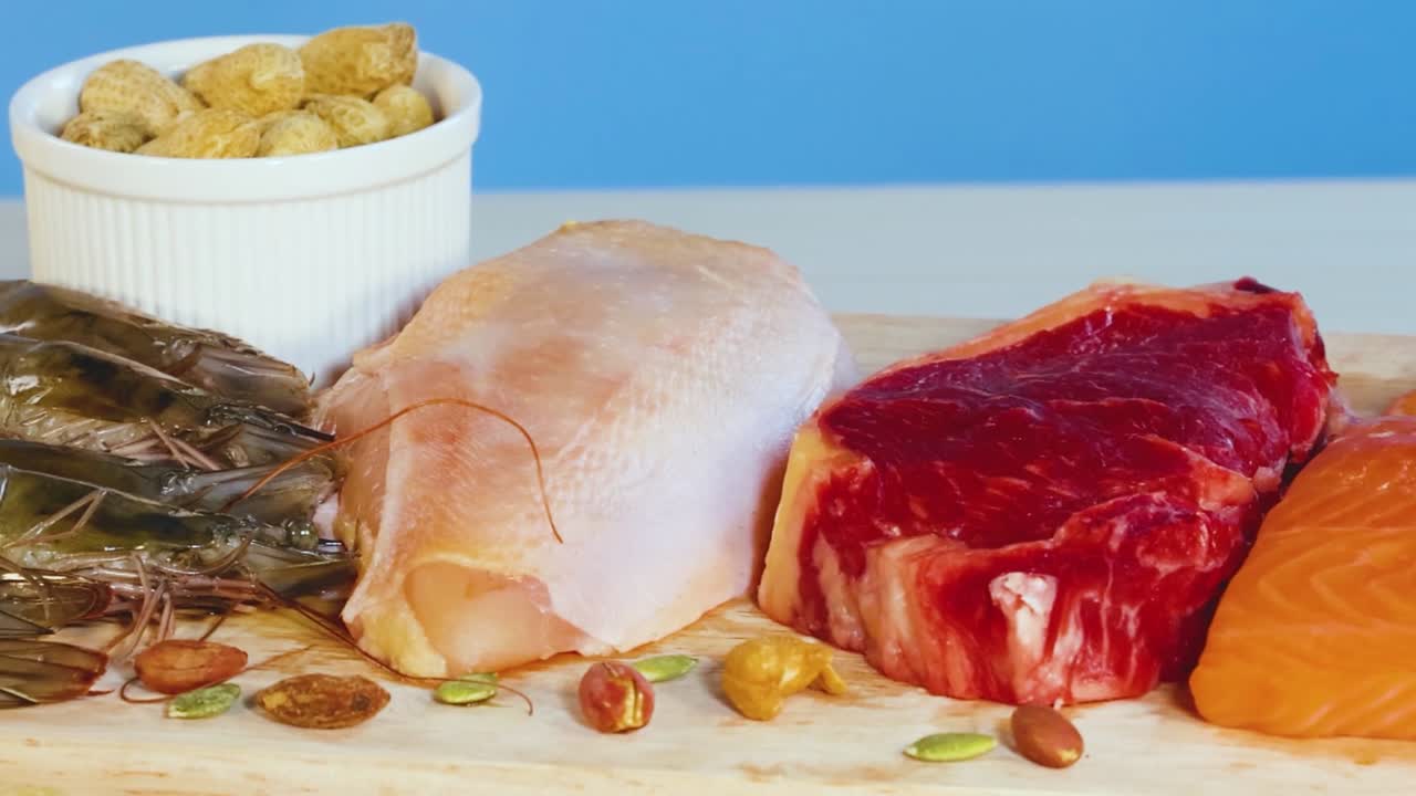 An assortment of meats, seafood, and nuts displayed on a wooden board with a blue background.