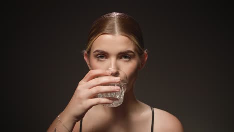 Una-Mujer-Sedienta-Bebe-Agua-De-Un-Vaso-Transparente,-Fondo-Negro