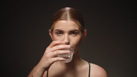 thirsty woman drinks water from a transparent glass, black background