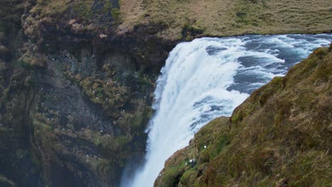 Former-coastline-edge-with-Skogafoss-waterfall-dropping-down-from-cliff,-Iceland