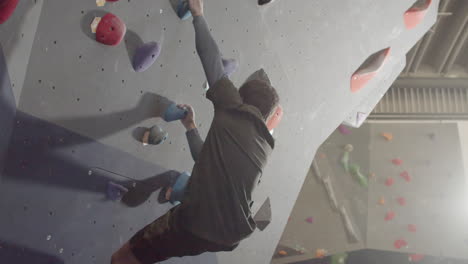 young male athlete climbing artificial rock wall in bouldering gym