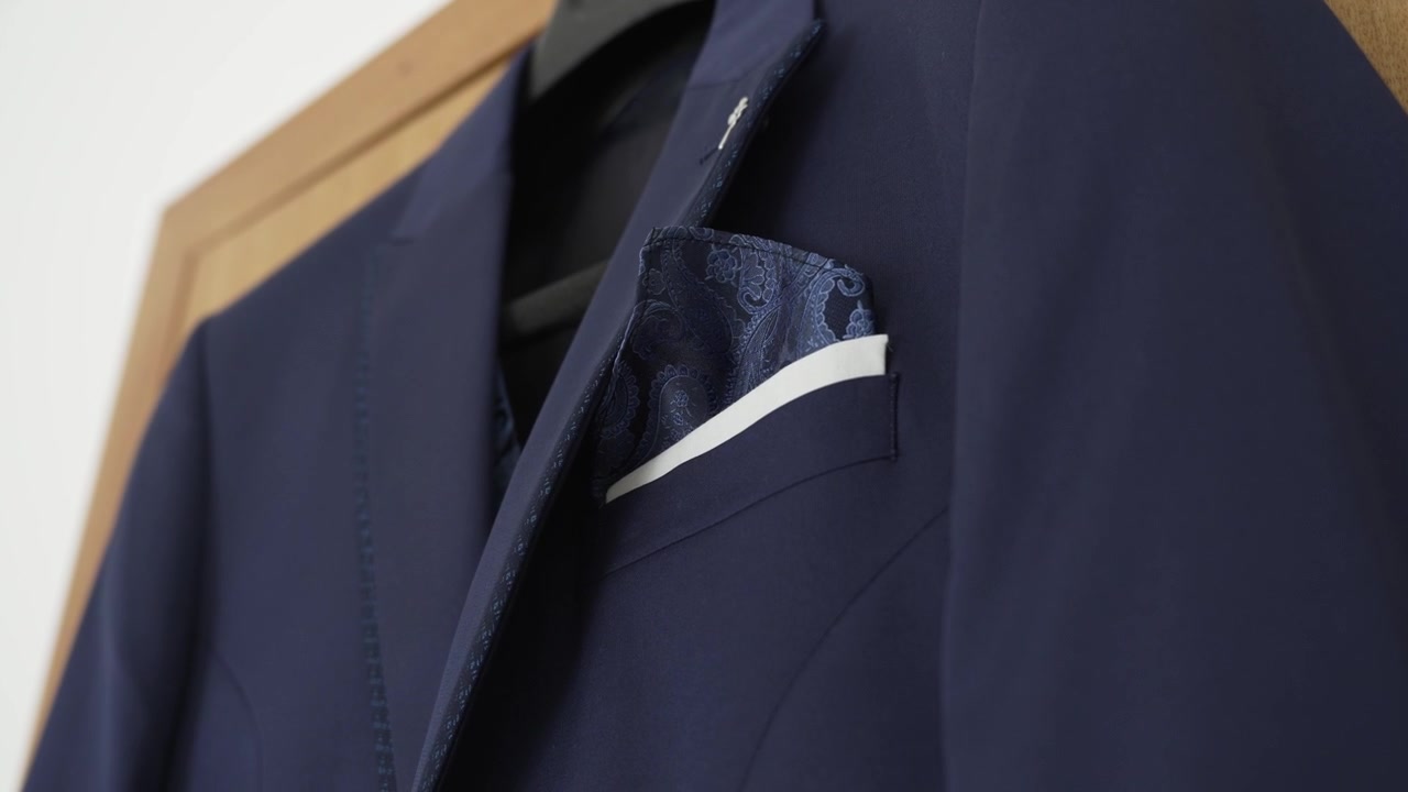 Elegante giacca da completo blu navy con fazzoletto da taschino bianco e dettaglio paisley in primo piano.