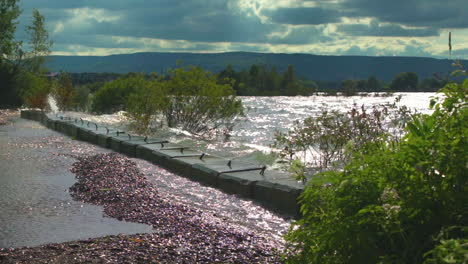 High-waves-crash-into-bulwark-in-slow-motion,-sending-water-flying-onto-a-walkway