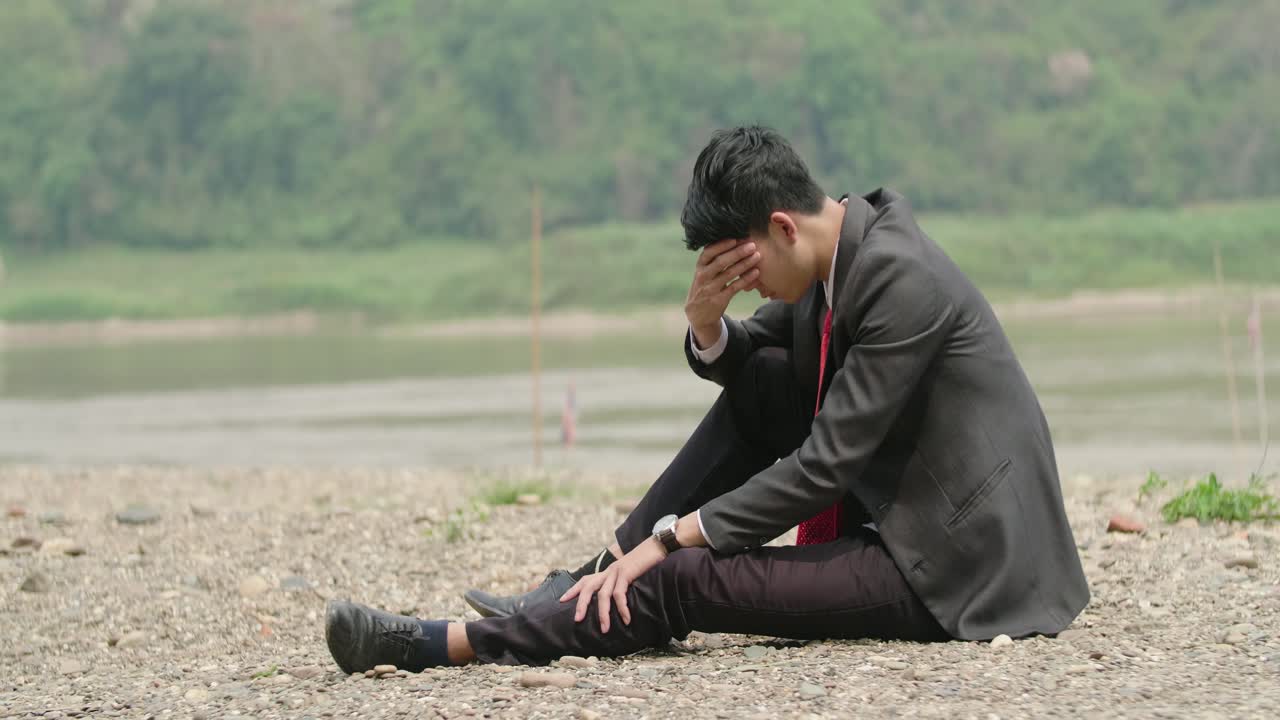 Businessman Sitting by River in Distress
