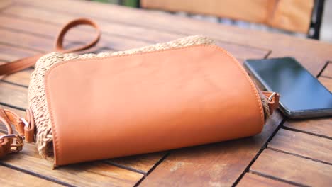brown straw shoulder bag on wooden table with a mobile phone