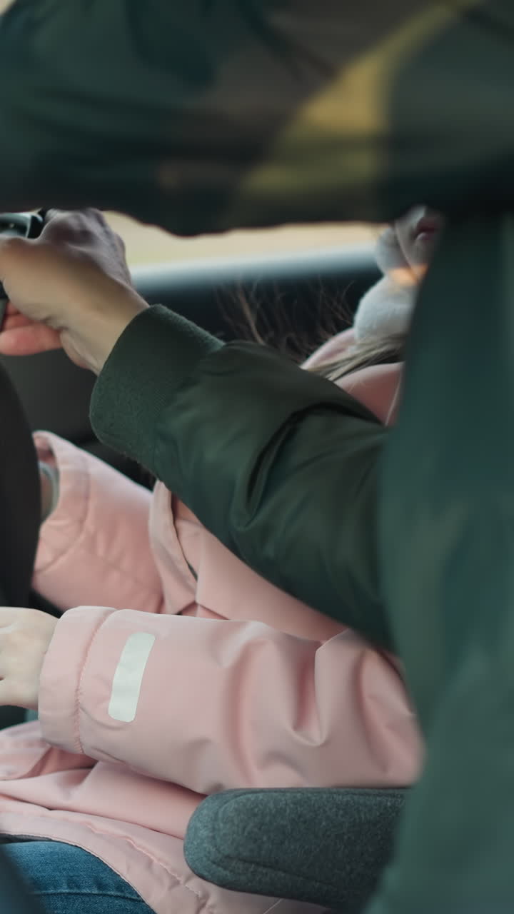 초록색 재을 입은 남자가 핑크색 재과 베니를 입은 어린 딸을 위해 안전벨트를 고정하고 있습니다. 아이는 그녀의 안전을 보장하는 동안 아버지에게 주의 깊게보고 있습니다.