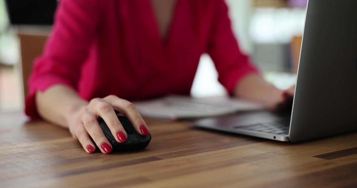 Una mano femminile clicca il mouse del computer su una moderna scrivania in legno da ufficio.