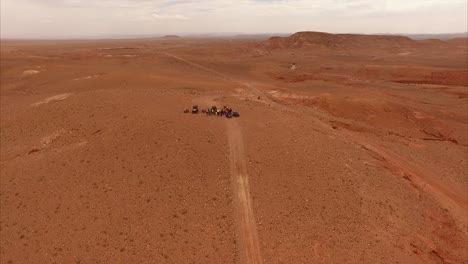 aerial shot moving away from a group of quads in the middle of desert