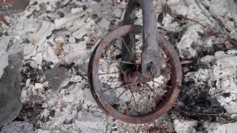 aerial of abandoned kid's bike in the middle of the ash remains of a burnt structure - aftermath of wildfire - 4k