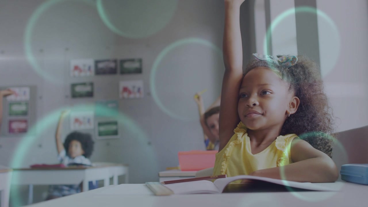 Girl raising hand after teacher cue in classroom, talking to answer while bokeh floats across book