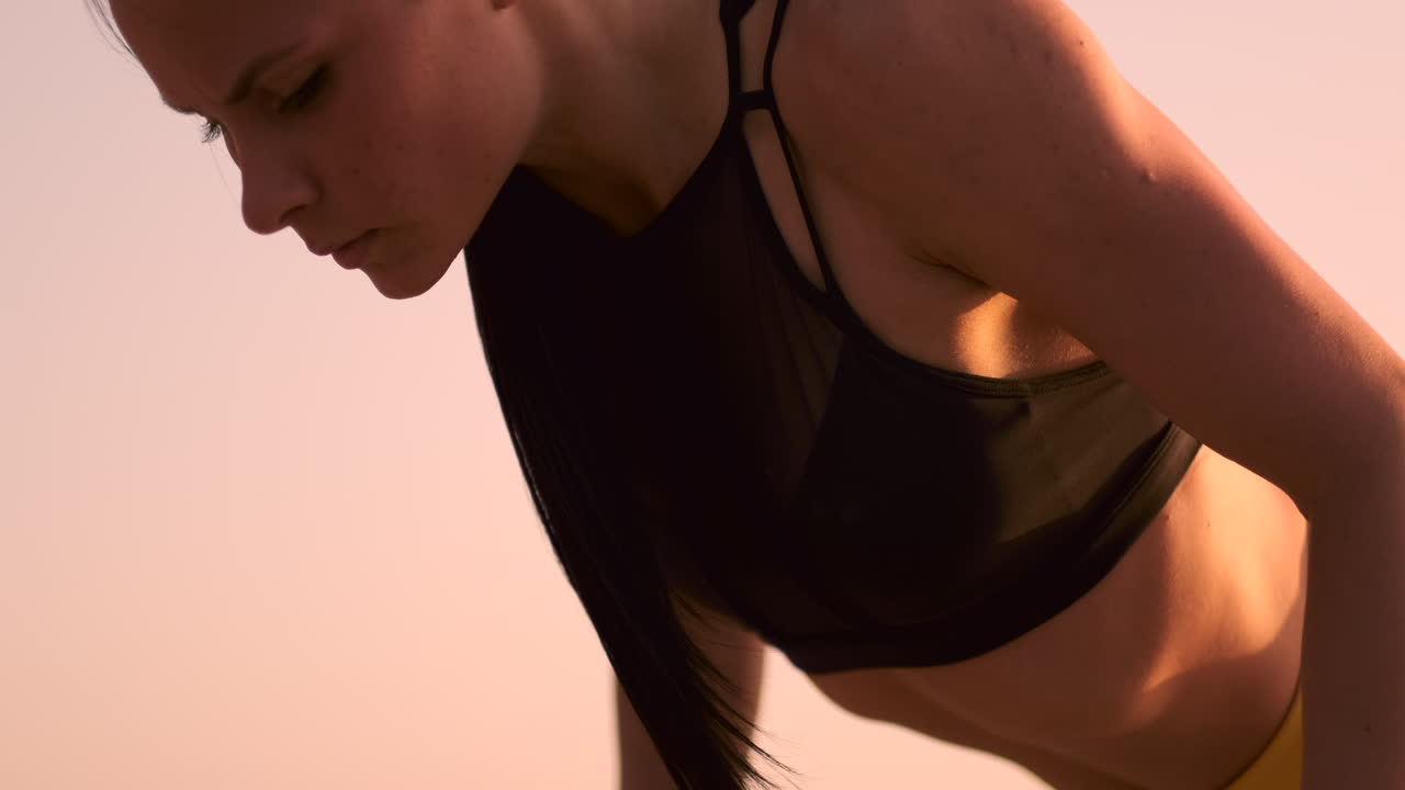 Bella atleta snella con un top nero e pantaloni gialli, al tramonto, esegue flessioni sulle parallele al rallentatore