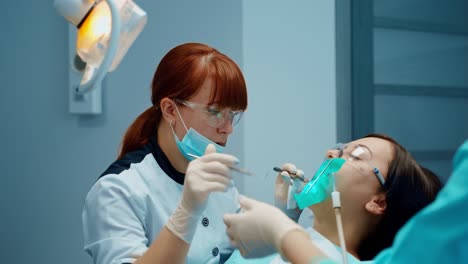 professional dentist treats patient's teeth. woman sitting in a dental chair with opened mouth in modern stomatology office. nurse gives instruments to a doctor.