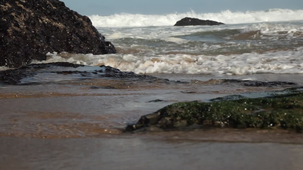 Ocean waves crashing onto the beach. Green carpet of moss covering the rocks. Cresmina beach (Praia da Cresmina), Portugal.
