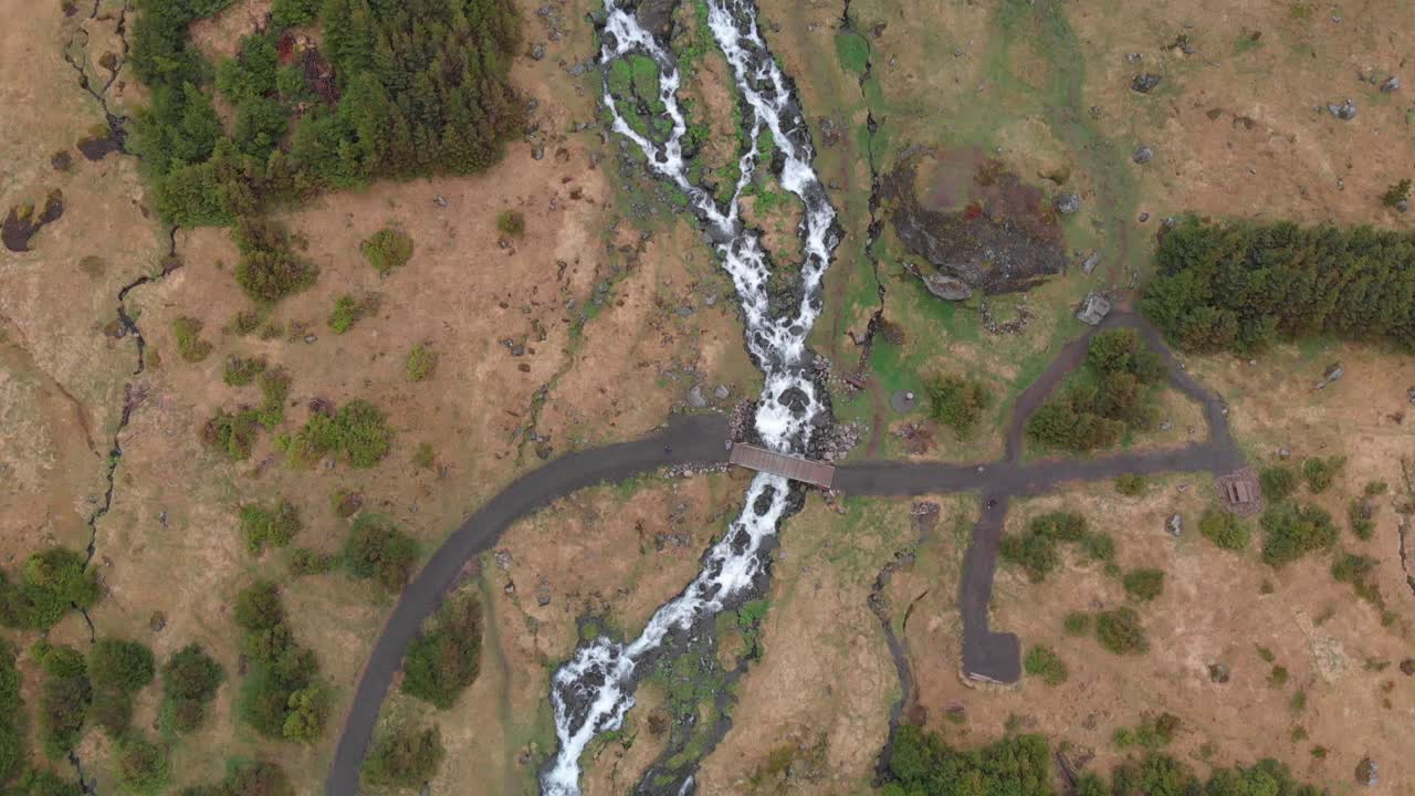 Aerial video going straight over the river flowing from the tall and wonderful waterfall Bjarnarfoss in the western part of Iceland with the lush bush landscape around it