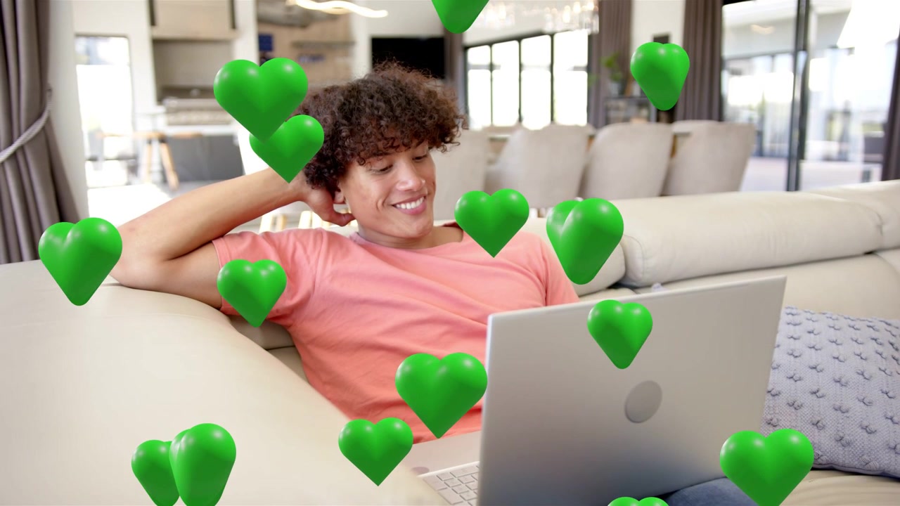 Beim Abspielen erscheinen grüne Herzen, Mann entspannt auf Sofa mit Laptop, Herzen schweben für Marketingzwecke über den Schoß.