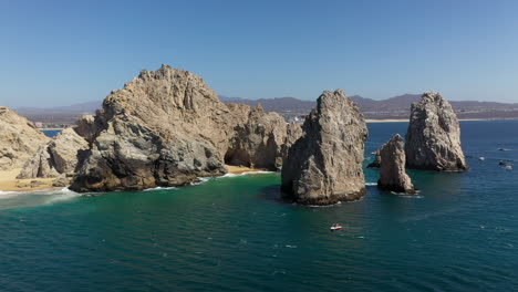 Drone-shot-of-Playa-del-Amor-and-El-Arco-natural-sea-cliffs-with-boats-in-the-ocean-in-Cabo-San-Lucas-Mexico,-wide-and-rotating