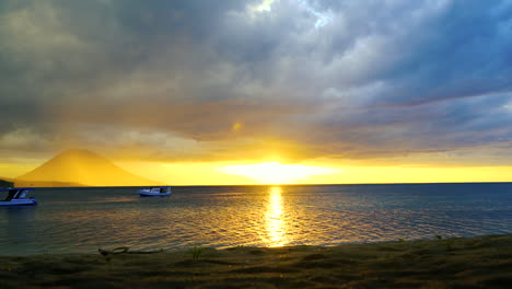 Hermoso-Lapso-De-Tiempo-Que-Muestra-Un-Volcán-En-El-Fondo-Y-Un-Barco-De-Buceo-PADI-En-Primer-Plano-Con-Un-Cielo-Ardiente-Mientras-Se-Pone-El-Sol.