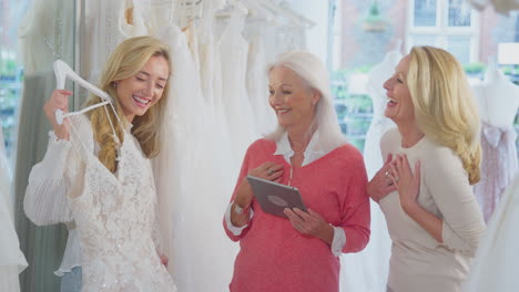 sales assistant with mother helping adult daughter to choose wedding dress in bridal store