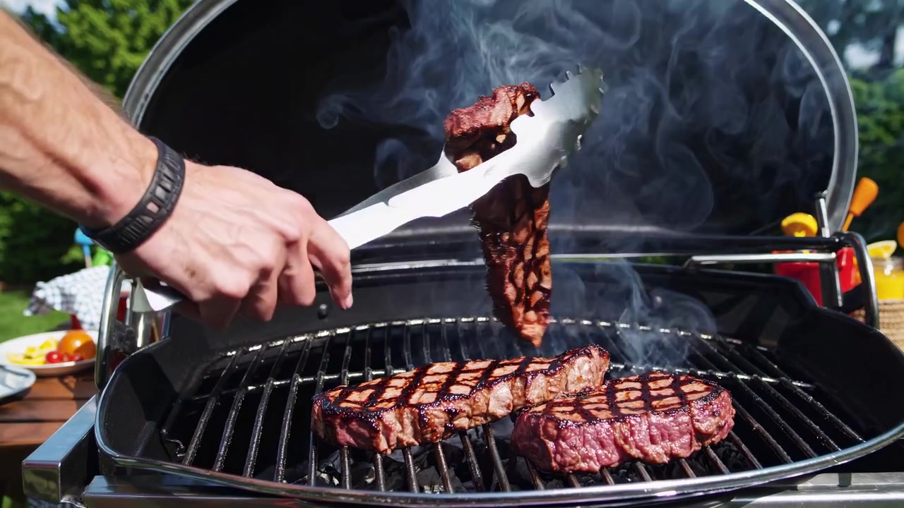 Uomo che gira le bistecche su una griglia calda per barbecue in un giardino estivo