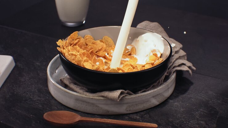SUPER SLOW MOTION Milk is being poured into a bowl with golden yellow crispy cornflakes, healthy breakfast. Shot with high speed camera at 420 FPS